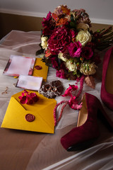 wedding accessories: a bride’s bouquet of roses, peonies and hydrangeas, wedding rings on a stone, a ring and earrings with diamonds, women's shoes, invitation and yellow envelopes with a red wax seal