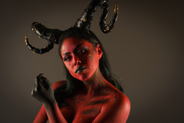 young pretty girl doing body painting characterized by demon with big black horns and red and black...