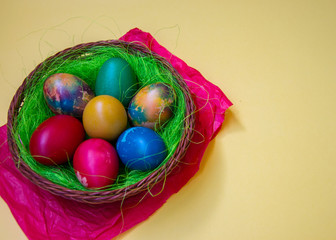 Green grass nest in a basket with colored chicken Easter eggs, multicolored painted eggs, Easter tradition, copy space, empty place for text, celebration concept 