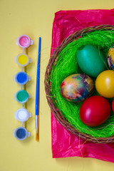 Green grass nest in a basket with colored chicken Easter eggs, multicolored painted eggs and paints, Easter tradition, celebration concept 