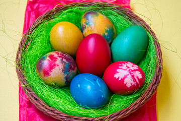 Fototapeta na wymiar Green grass nest in a basket with colored chicken Easter eggs, multicolored painted eggs, Easter tradition, celebration concept 