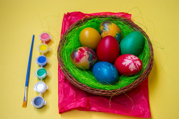 Green grass nest in a basket with colored chicken Easter eggs, multicolored painted eggs and paints, Easter tradition, celebration concept 
