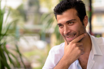 Face of happy handsome Turkish man thinking at the coffee shop