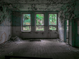 An empty, derelict room with broken windows, looking out on a green forest 
