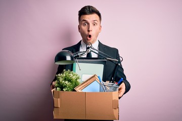 Young handsome caucasian business man holding cardboard box unemployment fired from job scared in shock with a surprise face, afraid and excited with fear expression - obrazy, fototapety, plakaty
