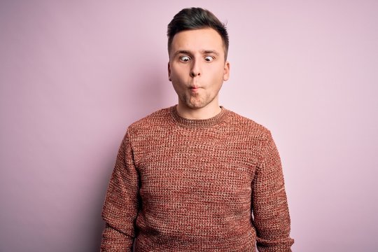 Young handsome caucasian man wearing casual winter sweater over pink isolated background making fish face with lips, crazy and comical gesture. Funny expression.
