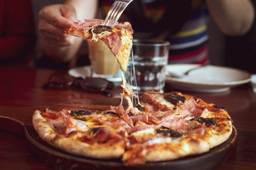 closeup hand with knife and fork on delicious pizza with chesse and ham, mushrooms on a wooden table