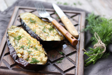 Grilled eggplant with dill and butter on a brown wooden board with a fork and knife on a grey wooden background. Bunch of herbs. Rustic. Background image, copy space