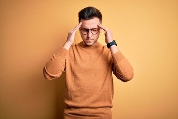 Young handsome caucasian man wearing glasses and casual winter sweater over yellow background with hand on head for pain in head because stress. Suffering migraine.
