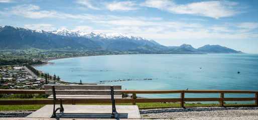 Beautiful vista shot of coastal town with azure waters, mountains in backdrop and bench in...