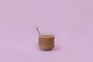 Cup of coffee with milk and a spoon on a pink background.