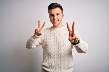 Young handsome caucasian man wearing casual winter sweater over white isolated background smiling looking to the camera showing fingers doing victory sign. Number two.