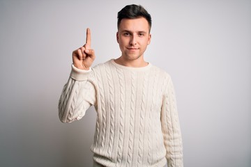 Young handsome caucasian man wearing casual winter sweater over white isolated background showing and pointing up with finger number one while smiling confident and happy.