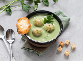 Soup-puree of greens with meatballs with croutons in a bowl on a light background