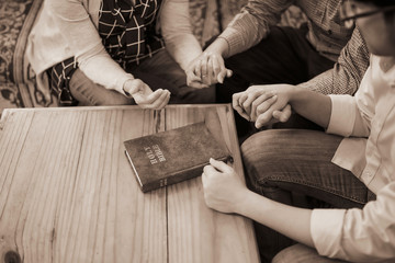 Close up of  people group holding the hand and pray together over a holy bible on wooden table,...