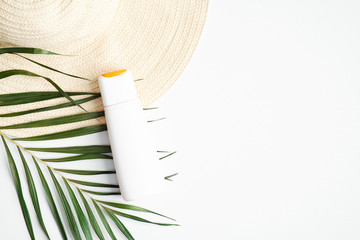 Sunscreen cream bottle on white background with female beach hat and tropical palm leaf. Flat lay,...