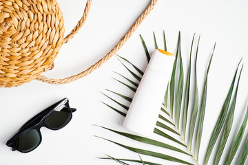 Suntan lotion bottle on white background with female rattan handbag, sunglasses, tropical palm leaf. Summer background. Travel, holiday, vacation concept. Flat lay, top view