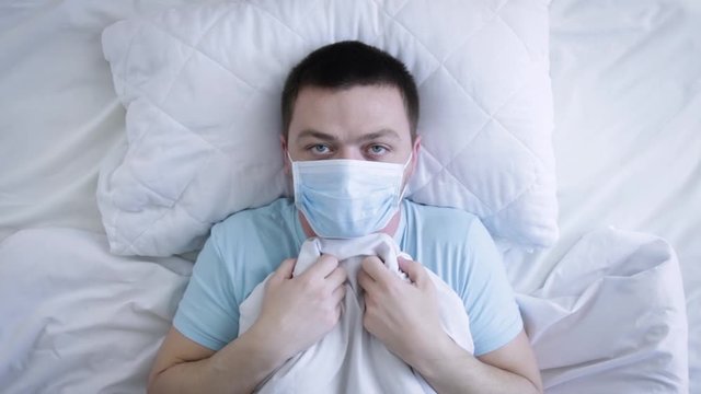 Man In Medical Mask In The Bed. Sick Man With Medical Mask Suffering From Sore Throat. Coronavirus  Covid-19. Health Concept