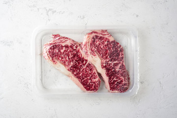 Raw Wagyu steak of marbled beef in vacuum packaging on a white stone background