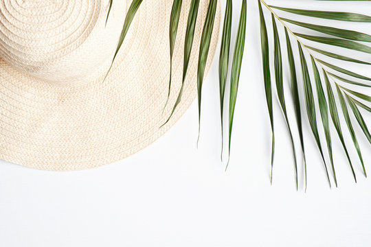 Straw beach hat with tropical palm leaf on white background. Travel, holiday, vacation concept. Flat lay, top view
