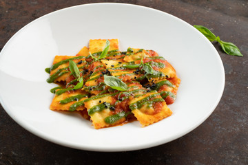 Cooked ravioli with tomatoes, pesto sauce and Basil leaves on a white plate, close-up