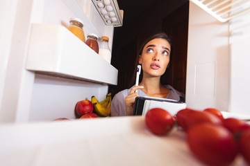 Woman inspecting refrigerator and making shopping list