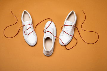 Three white sport sneaker shoes connected with a red lace on yellow background