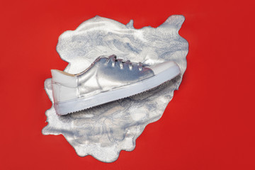 White sport sneaker shoe in a puddle of silver paint shot from above on red background