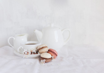 Obraz na płótnie Canvas Tasty French macarons and a tea-set with blossoming branches on a white background.