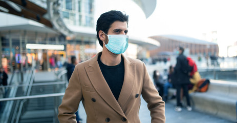 Handsome man walking outdoors in a crowded street while wearing a mask
