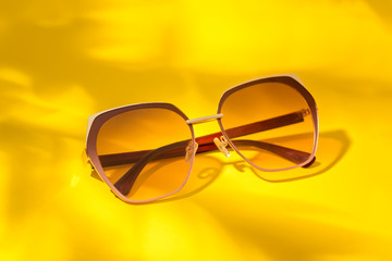 Stylish sunglasses on yellow background, top view