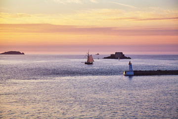 An old sailboat enters the Bay of Saint Malo at sunset. France. Brittany