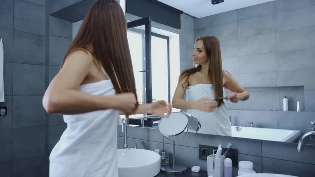 happy young woman combing hair in front of mirror in bathroom