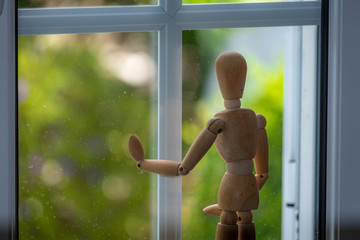 Isolado boneco de madeira articulado à janela a olhar para o exterior