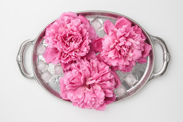 Obraz na płótnie Canvas Three pink peony flowers with ice on a metal tray