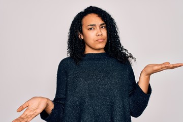 Young african american curly woman wearing casual sweater standing over white background clueless...