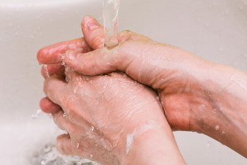 Man's hand under the tap with water. Wet hands and spray of water. Personal hygiene and prevention of coronavirus disease.