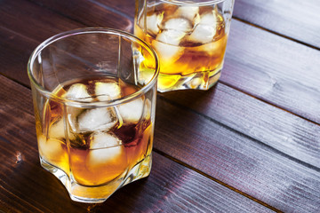 Two glasses of whiskey with ice cubes served on wooden planks.