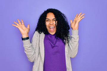 Young african american sporty woman wearing casual sweatshirt over purple background celebrating crazy and amazed for success with arms raised and open eyes screaming excited. Winner concept