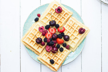 Belgian waffles with strawberry, cherry, blueberry on blue plate. White background.