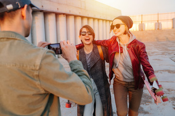 Man taking pictures of two young happy short-haired women with skateboards