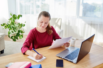 Portrait of young confident business woman sitting at wood desk and writing plan in notebook at home office, copy space