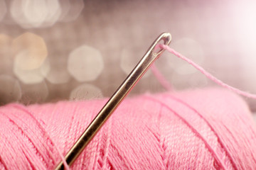 A macro image of a needle s eye threaded, pink thread