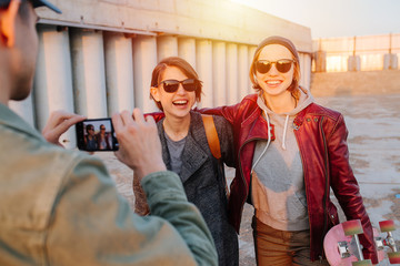 Man taking pictures of two young happy short-haired women with skateboards
