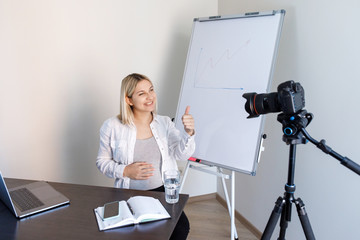 Online education, educational blogging. A young pregnant woman tutor records training video lessons to the camera, she stands and shows with a pen on a flip chart with graphs and diagrams