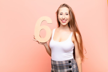 yound blonde woman excited, happy, joyful, holding a number 6.