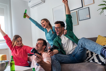 Group of friends having fun sitting on sofa in living room and playing video games at home.
