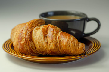 Delicious croissant on a plate with coffee in a cup