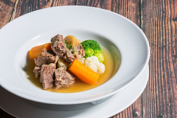 Vegetables cooked with veal meat in white plate on wooden table