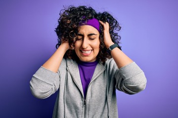 Beautiful curly arab sportswoman doing sport wearing sportswear over purple background suffering from headache desperate and stressed because pain and migraine. Hands on head.